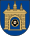 A coat of arms depicting a grey castle with three towers topped by crosses with a human head on the front door all on a blue background