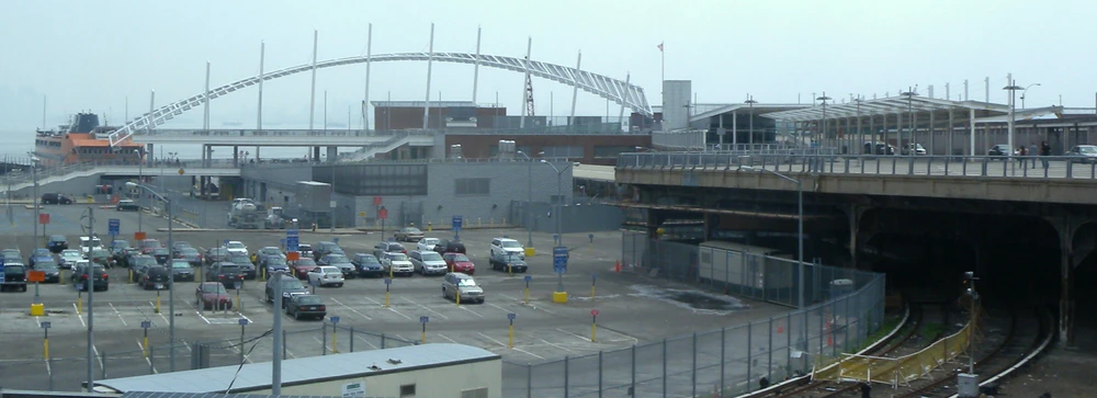 Терминал Сент-Джордж (паромный, железнодорожный и автобусный), вид с улицы Ричмонд-Террас (снимок 2010 года). Рельсы на переднем плане ведут от платформ терминала (справа под мостом) в сторону закрытой станции Боллпарк (слева за пределами кадра). На мосту над платформами находятся автобусные остановки. Слева за стоянкой (сейчас её территория застроена) виден пришвартованный паром