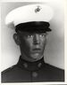 Head of a young white man wearing a white peaked cap with black visor and a dark military jacket with a pin on each side of the upright collar.