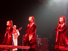 YUIMETAL, SU-METAL, и MOAMETAL в чёрных кимоно с лицами, закрытыми маской лисы, выступая на сцене